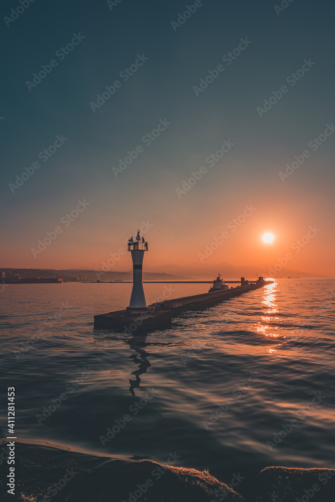silhouette of a lighthouse standing on the pier at sunset