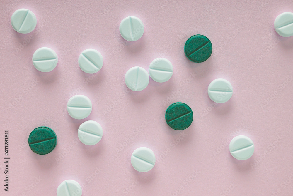 White and green pills lie on a sheet of pink paper. Close up. Light background or backdrop on the theme of medicine, health care, drugs, pharmacology. Tablets of different colors. View from above White and green pills lie on a sheet of pink paper. Close up. Light background or backdrop on the theme of medicine, health care, drugs, pharmacology. Tablets of different colors. View from above