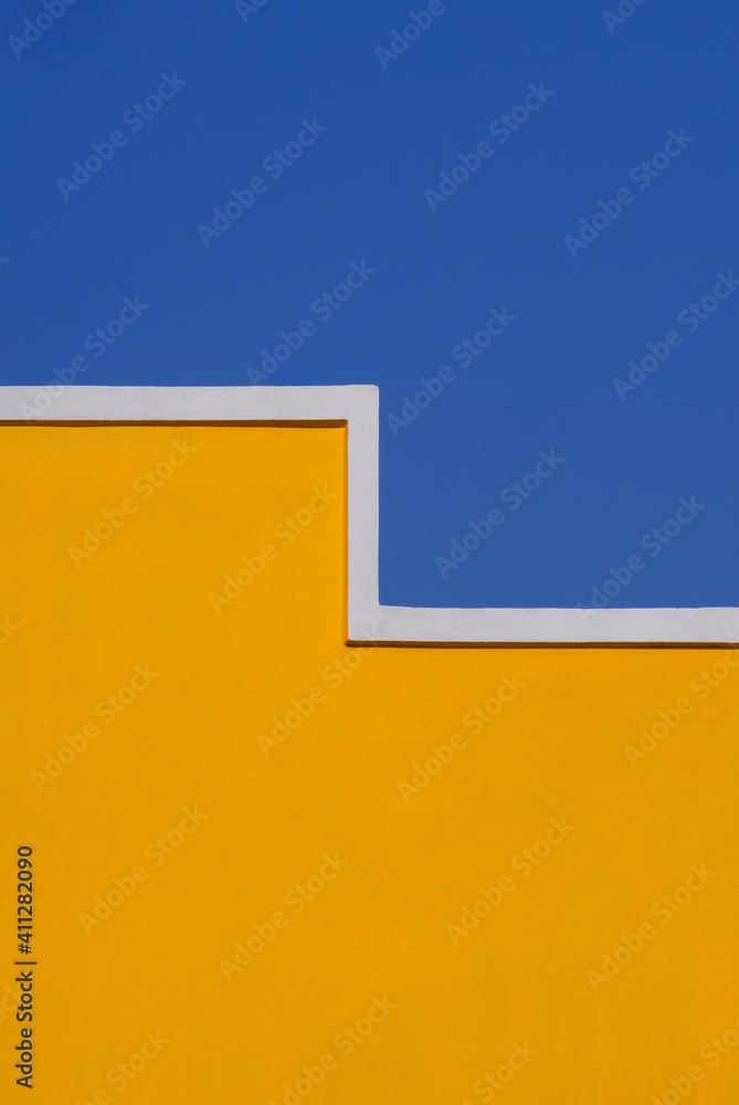 Geometric shape of empty yellow cement building wall against blue clear sky in vertical frame for architecture and background design concept Geometric shape of empty yellow cement building wall against blue clear sky in vertical frame for architecture and background design concept