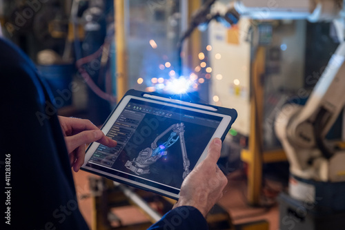 Manager industrial engineer using tablet check and control automation robot arms machine for build a part of product.