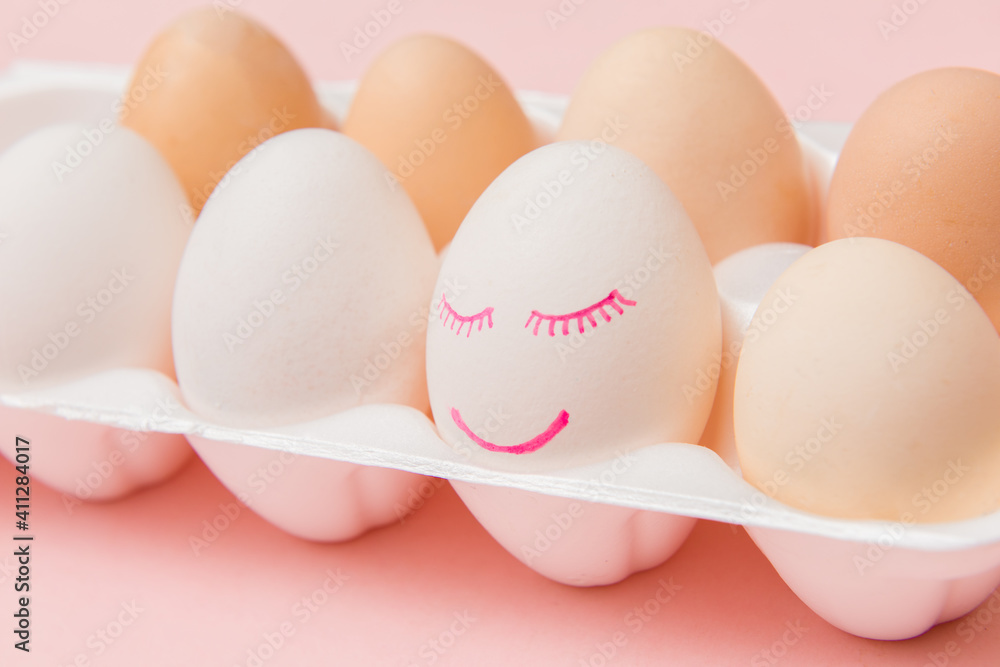 White chicken egg with painted face and smile in pink egg box. Happy Easter concept White chicken egg with painted face and smile in pink egg box. Happy Easter concept