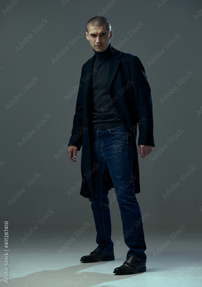 Portrait of handsome brave young man dressed in black coat stylish businessman on gray studio background