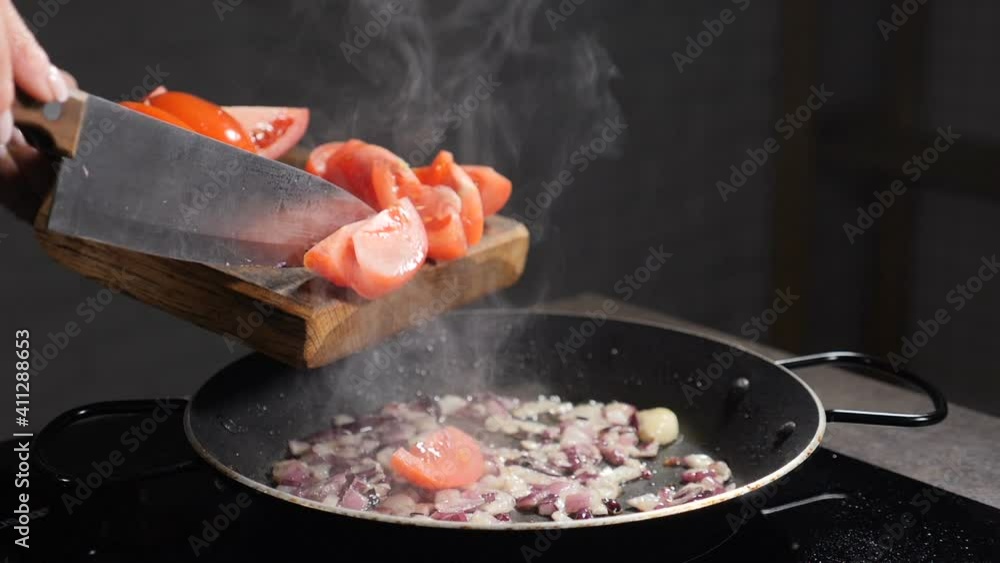 Adding sloced tomato into pan with frying onion, oil splashing. Cooking process. Tomatoes in hot pan are fried at home in kitchen, close-up. Cooking sauce. Slow motion. Full hd Adding sloced tomato into pan with frying onion, oil splashing. Cooking process. Tomatoes in hot pan are fried at home in kitchen, close-up. Cooking sauce. Slow motion. Full hd