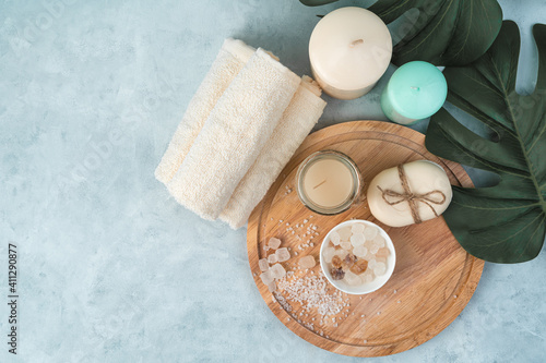 Candles, towels, soap, salt on a wooden board on a light blue background with monstera leaves. Top view with copy space. The concept of spa treatments.