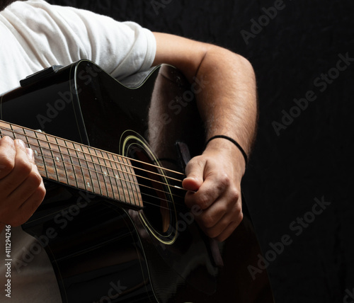 Young man playing guitar, close up view, dark background.
