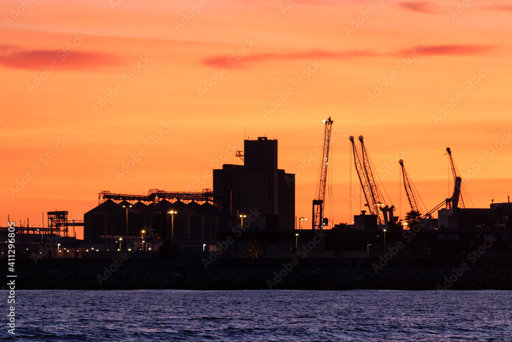 Cranes, silos and warehouses at an industrial harbor, evening time, sunset at the port. Tarragona by the Mediterranean sea, Catalonia, Spain