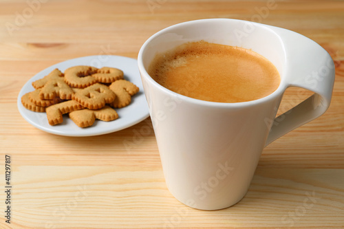 Closeup a cup of hot frothy coffee with plate of cookies on wooden table 