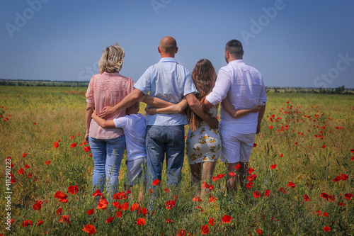 A family of five stands on a day in a poppy fieldwith their backs to the camera. friendly family, family reunification