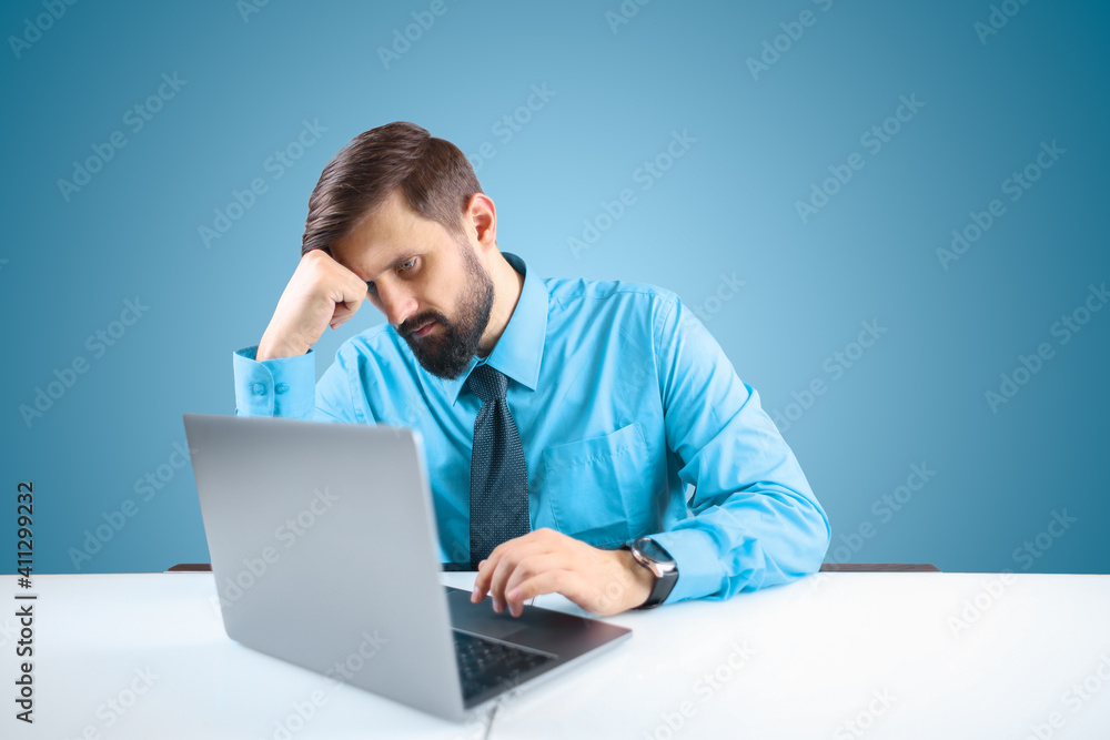 a businessman in a blue shirt and tie is working thoughtfully at a computer on a responsible project, the man leaned his hand to his head, thinking about work a businessman in a blue shirt and tie is working thoughtfully at a computer on a responsible project, the man leaned his hand to his head, thinking about work