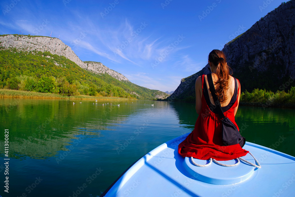Young woman sitting on the front of a boat admiring the view - holiday concept