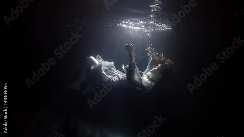 silhouette of sinking woman underwater, floating and diving under surface of dark pool