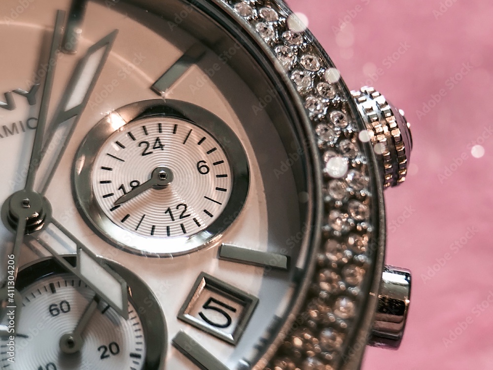 Fashion watch with chronograph and rhinestones. Fragment of a dial of a silver watch on a pink background. Fashion watch with chronograph and rhinestones. Fragment of a dial of a silver watch on a pink background.