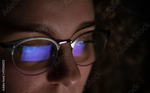 Computer screen reflected in the glasses of a woman who is working at night.