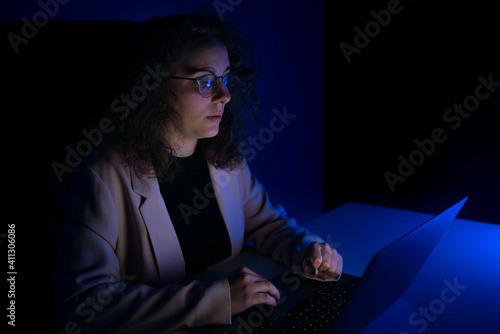Young woman typing on computer while it is night time. Blue lights.
