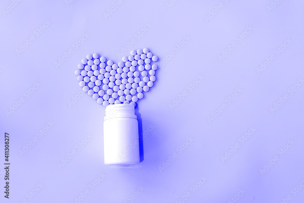 many small pills spilled out of a white jar on a purple background in the shape of a heart. many small pills spilled out of a white jar on a purple background in the shape of a heart.