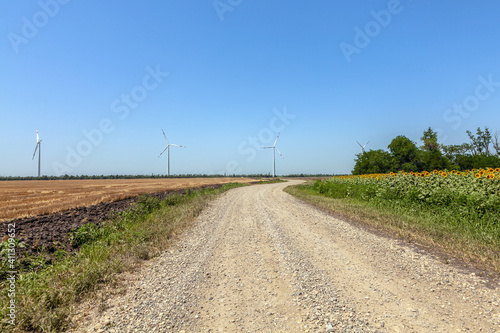 wind turbines on the background of a cloudy blue sky, view from a country road and sunflower fields
