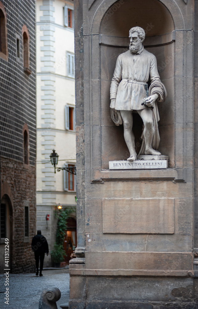 Fototapeta premium Florence, Italy - 2021, January 31: A view of the city, near the Uffizi museum courtyard. Benvenuto Cellini statue in the foreground. A man walking down the street.