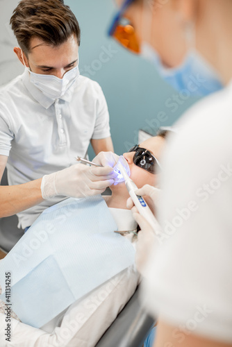Young dentist and assistant using dental curing UV light lamp during tooth treatment procedure. High quality photo