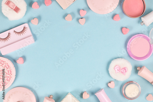 Cute pink makeup beauty products like brushes, powder or lipstick surrounding pastel blue background with empty copy space
