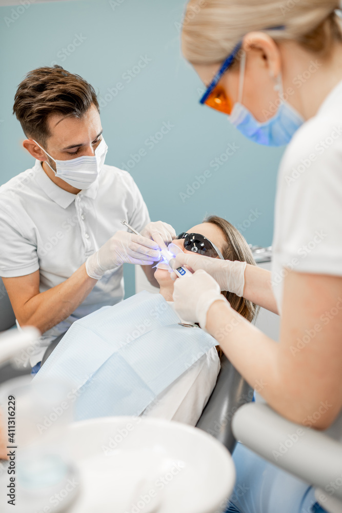 Young dentist and assistant using dental curing UV light lamp during tooth treatment procedure. High quality photo Young dentist and assistant using dental curing UV light lamp during tooth treatment procedure. High quality photo
