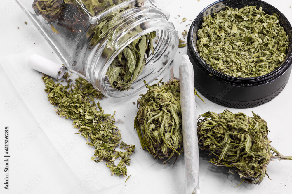 Fototapeta premium grinder full of dry herb and joint with medical marijuana with paper filter and piece of rolling paper on white background