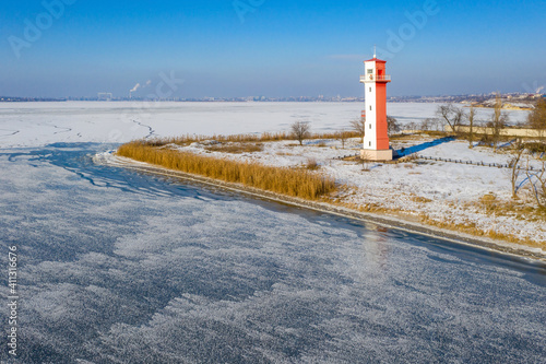 aerial view to lighthouse on the narrow spit in frozen river in winter day under blue sky in Ukraine