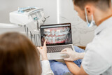 Dentist showing photo of teeth on a monitor for a young patient during an orthodontic treatment. Girl having a consultation with a orthodontist. High quality photo