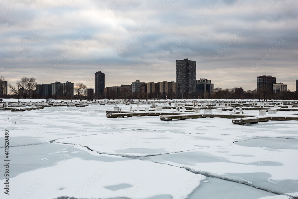 Naklejka premium Tall apartment buildings behind frozen marina with sheets of ice on cold winter day with overcast sky in urban Chicago