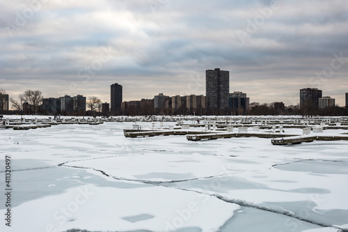 Tall apartment buildings behind frozen marina with sheets of ice on cold winter day with overcast sky in urban Chicago