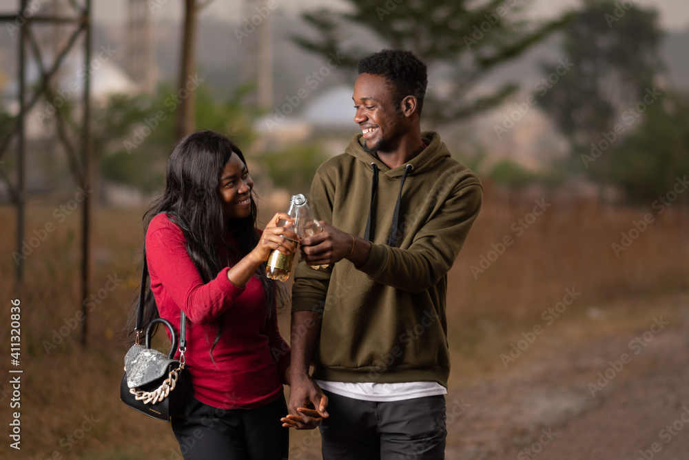 Fototapeta premium young african friends, couple walking and holding hands and having drinks, in happy mood