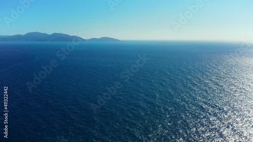 Drone facing the beautiful clear blue ocean in Alaties, Greece. Camera then point down towards the rocky shore, where waves hit. photo