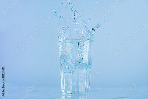 A glass of water splashed up. The water rose from a clear glass with a square.