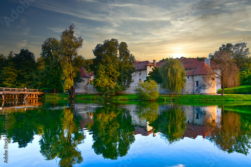 Castle Otočec on the river Krka in southern Slovenia, evening sunset scene with reflection of castle on the water