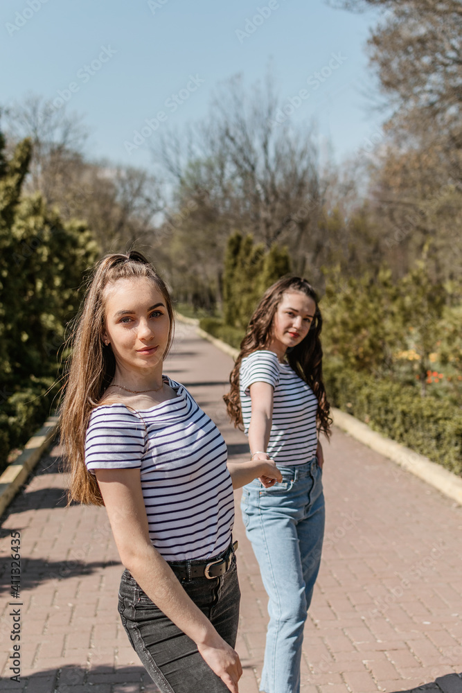 Gen z girls enjoying outdoors, expressing positive emotions. Outdoor photo of two girl friends having fun in the park. Two happy joyful young women jumping and laughing together
