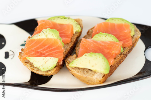 Homemade toast sandwich with salmon and avocado on a slice of cereal bread. The toast lies on a plate in the shape of a black and white panda. healthy food.