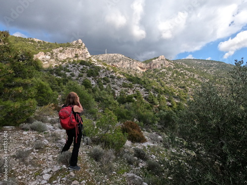 Woman hiker with red backpack photographing mountain scenery in Greece