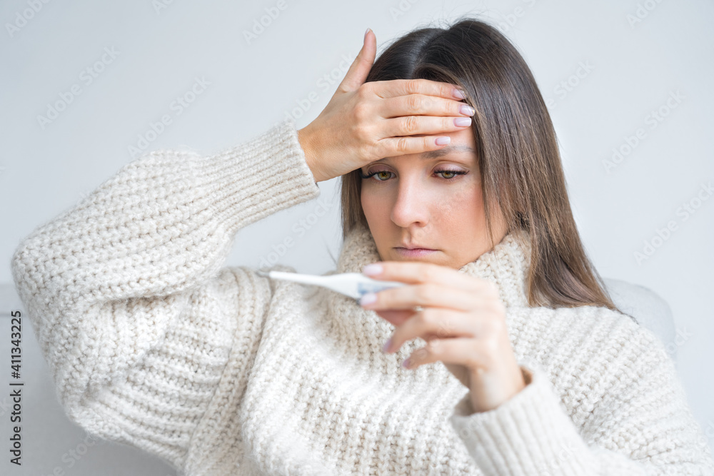 Sick unhealthy woman with fever holding a medical thermometer in her hand with high body temperature Sick unhealthy woman with fever holding a medical thermometer in her hand with high body temperature