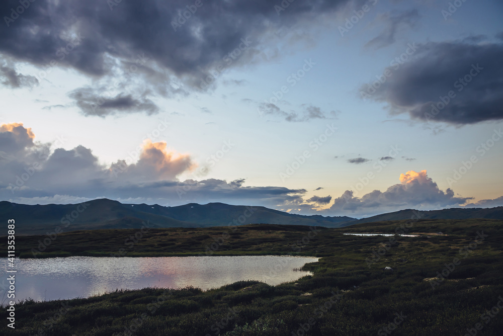 Fototapeta premium Scenic mountain scenery with lilac reflection of sunset in lake. Colorful mountain landscape with illuminating color in violet clouds in dawn gradient sky. Beautiful view to sunrise and lilac lake.