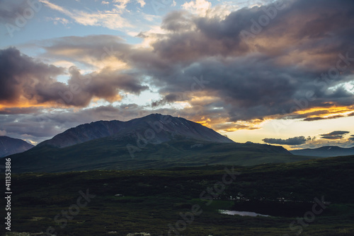 Beautiful mountain scenery with golden dawn light in cloudy sky. Scenic mountain landscape with illuminating color in sunset sky. Silhouettes of mountains on sunrise. Gold illuminating sunlight in sky