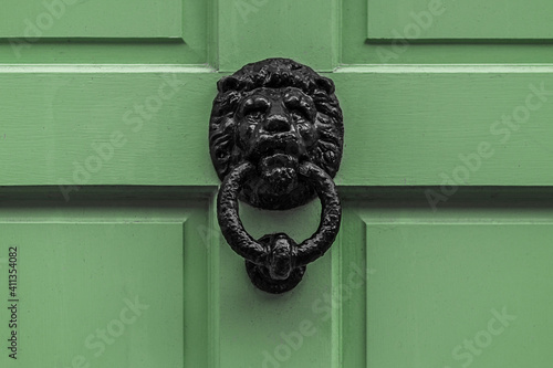 Generic old black cast iron lion head door knocker against a green painted wooden door shot straight on.