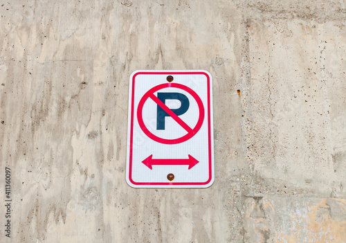 A no parking sign on a textured concrete wall with a directional arrow at the bottom of it