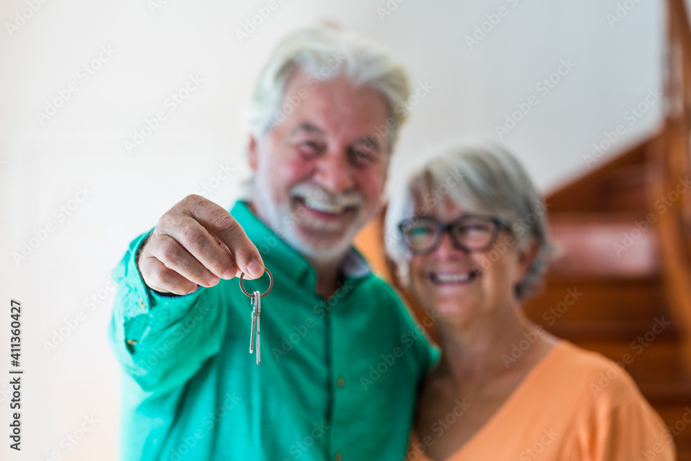 portrait and close up of two happy seniors buying a new house holding the key with his hand portrait and close up of two happy seniors buying a new house holding the key with his hand
