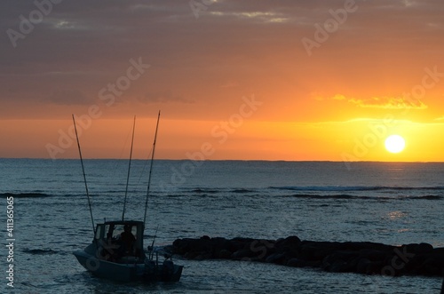 A fishing boat in the early morning sailing out towards the sunrise in the distance