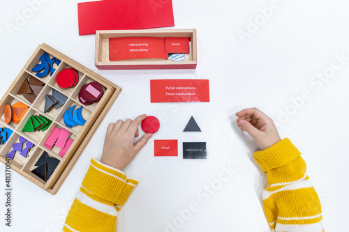 Top view of girls hand is sorting a puzzle of colored wooden geometric shapes in montessori school.