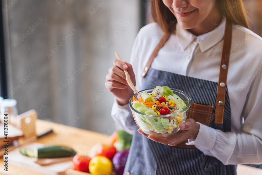 Closeup image of a beautiful young female chef holding and eating fresh mixed vegetables salad Closeup image of a beautiful young female chef holding and eating fresh mixed vegetables salad