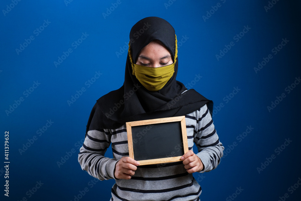 Portrait of young Asian woman wearing protective mask against the coronavirus, holding small blackboard Portrait of young Asian woman wearing protective mask against the coronavirus, holding small blackboard