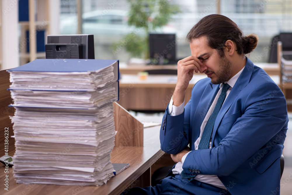 Young male employee unhappy with excessive work in the office Young male employee unhappy with excessive work in the office