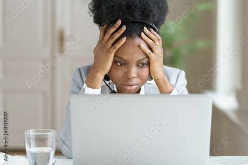 Obraz na plátně Portrait of tired annoyed afro businesswoman, wear headphones, talking to a bad customer looking at screen laptop in office
