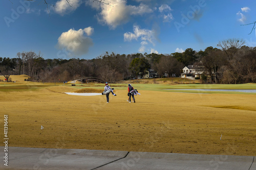 A majestic shot of a golf course with autumn colored grass surrounded by green and autumn colored trees with blue sky and clouds with people walking along the course playing golf at Tanyard Creek Park photo