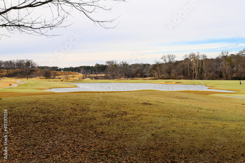 A majestic shot of a golf course with autumn colored grass surrounded by green and autumn colored trees with blue sky and clouds with people walking along the course playing golf at Tanyard Creek Park photo